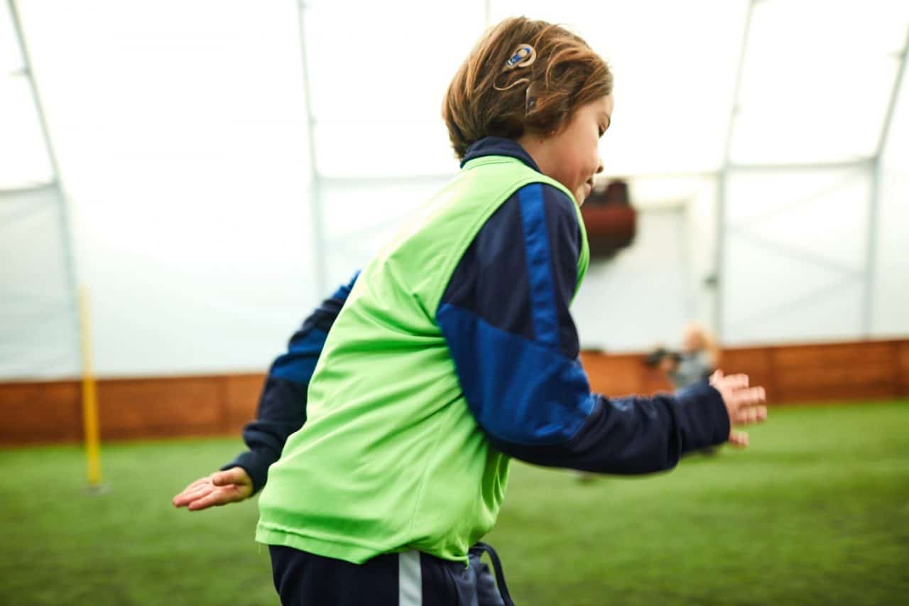 A child with a cochlear implant running on a sports field