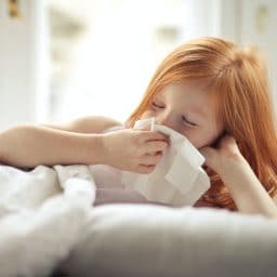 Young girl putting a tissue to her nose.