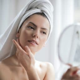 Woman rubbing lotion on her face after a shower.