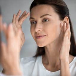Woman with smooth, clear complexion looking in the mirror.