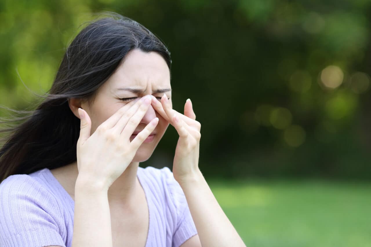 Woman holding her hands to her face experiencing sinus pain or pressure.